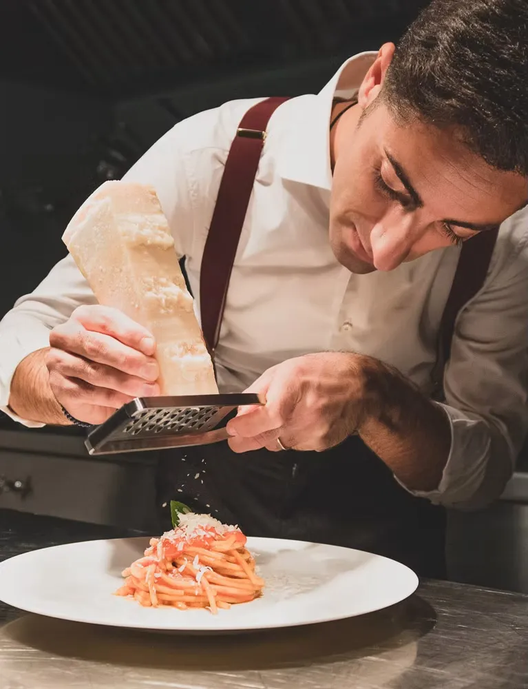 Federico Allegri grattugia il parmigiano su un piatto di pasta al pomodoro